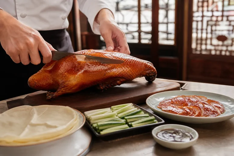 Chef carving Beijing roast duck beside pancakes, scallions, cucumber and sauce