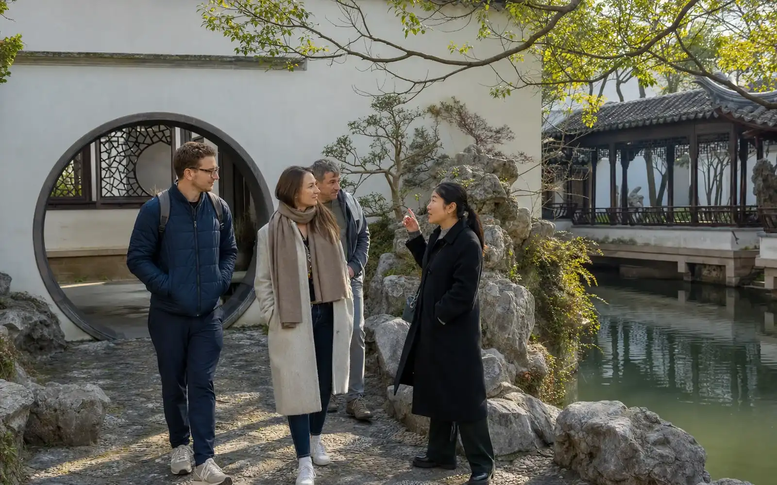 Travelers with a Suzhou guide in a classical garden beside white walls and a canal