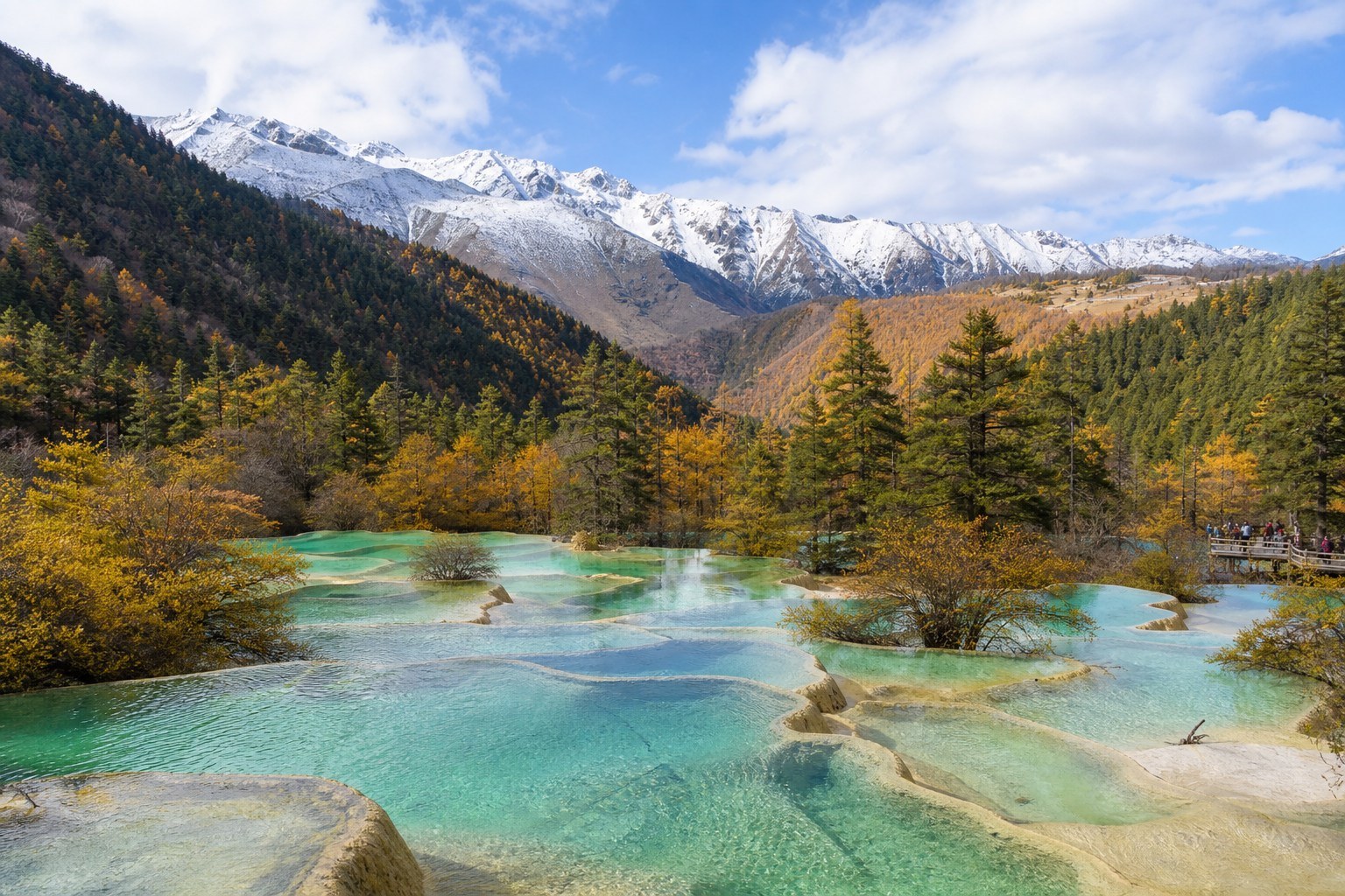 Clear turquoise travertine terraces among golden forest in Huanglong