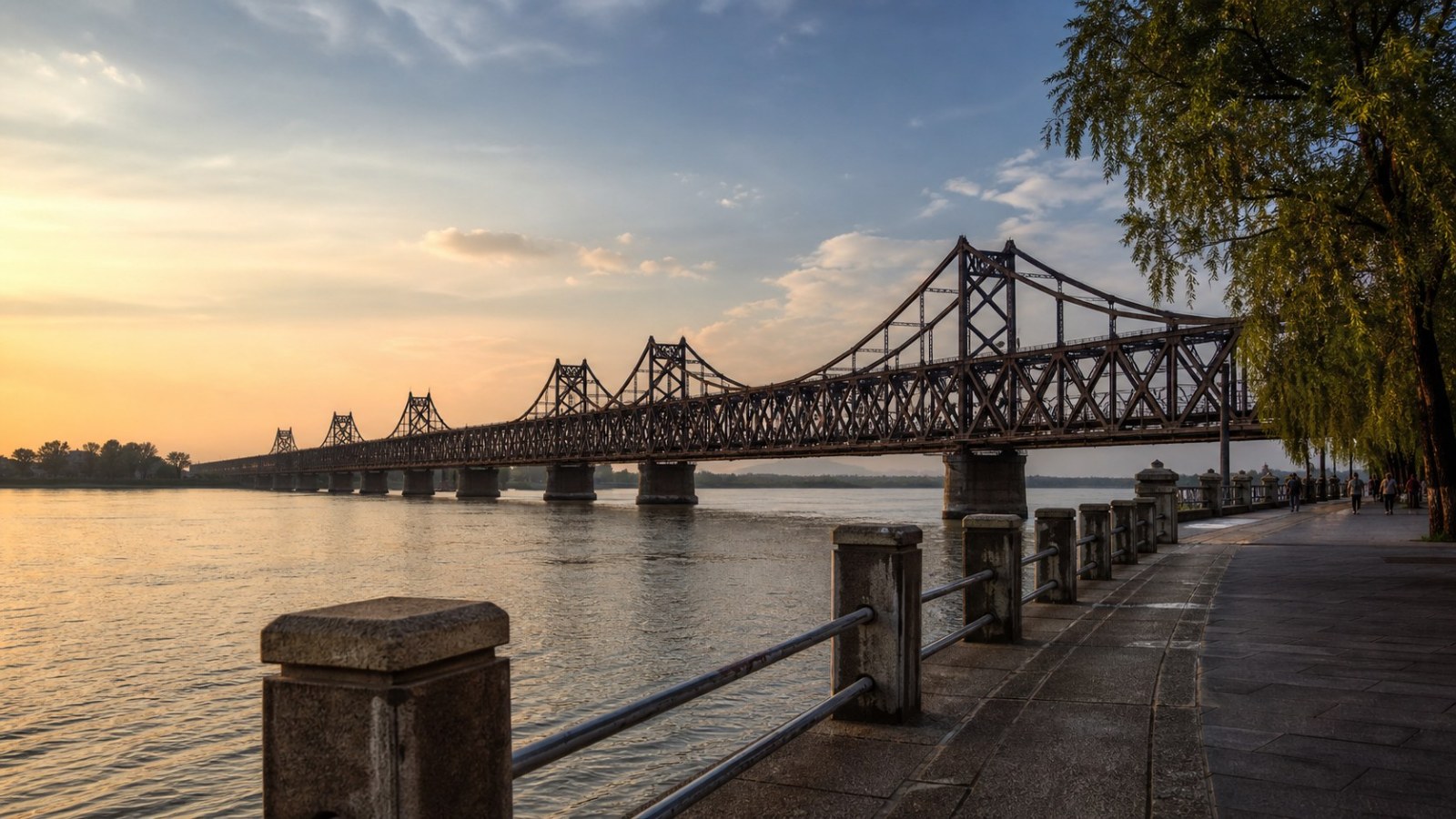 Dandong riverside promenade and historic steel bridge at golden hour