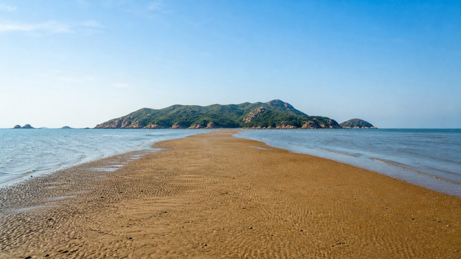Low-tide sand path leading toward a green island near Jinzhou