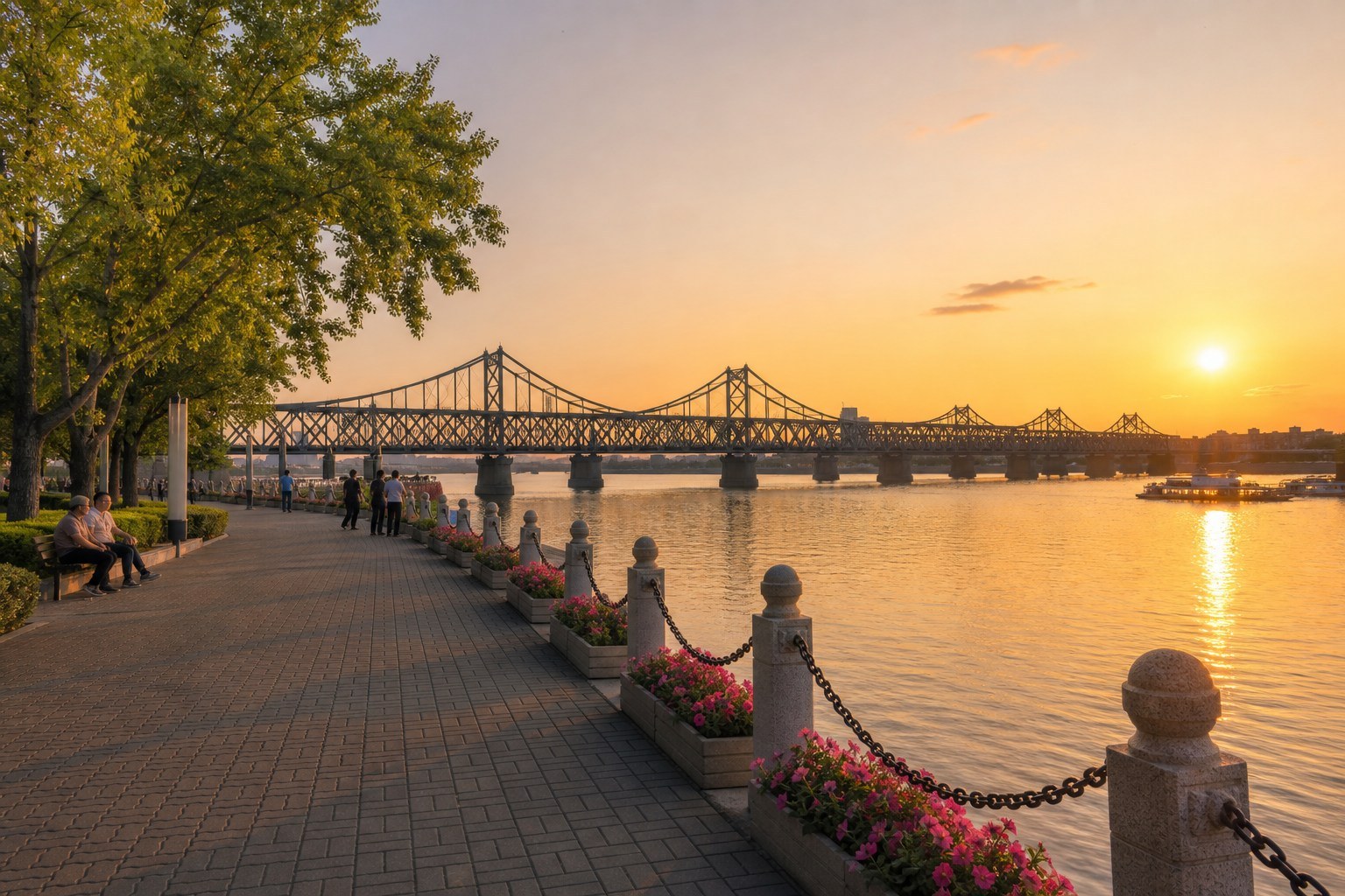 Landscaped Dandong promenade beside the Yalu River and historic steel bridge at golden hour