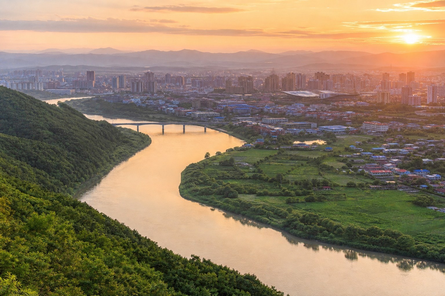 Tumen River valley, green hills and modern Yanji city in warm sunset light
