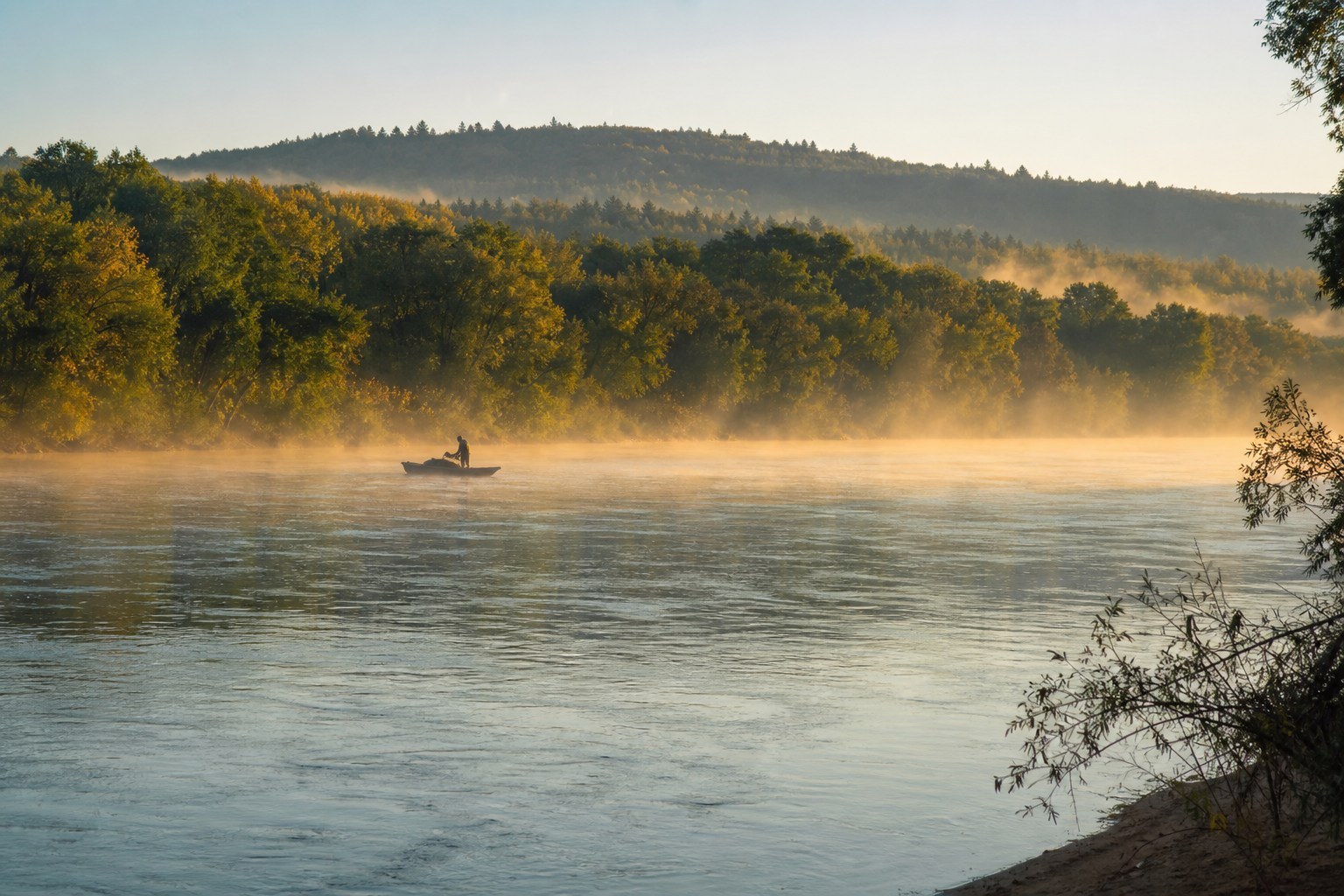 Ussuri River, forested banks and a distant wooden fishing boat in morning mist