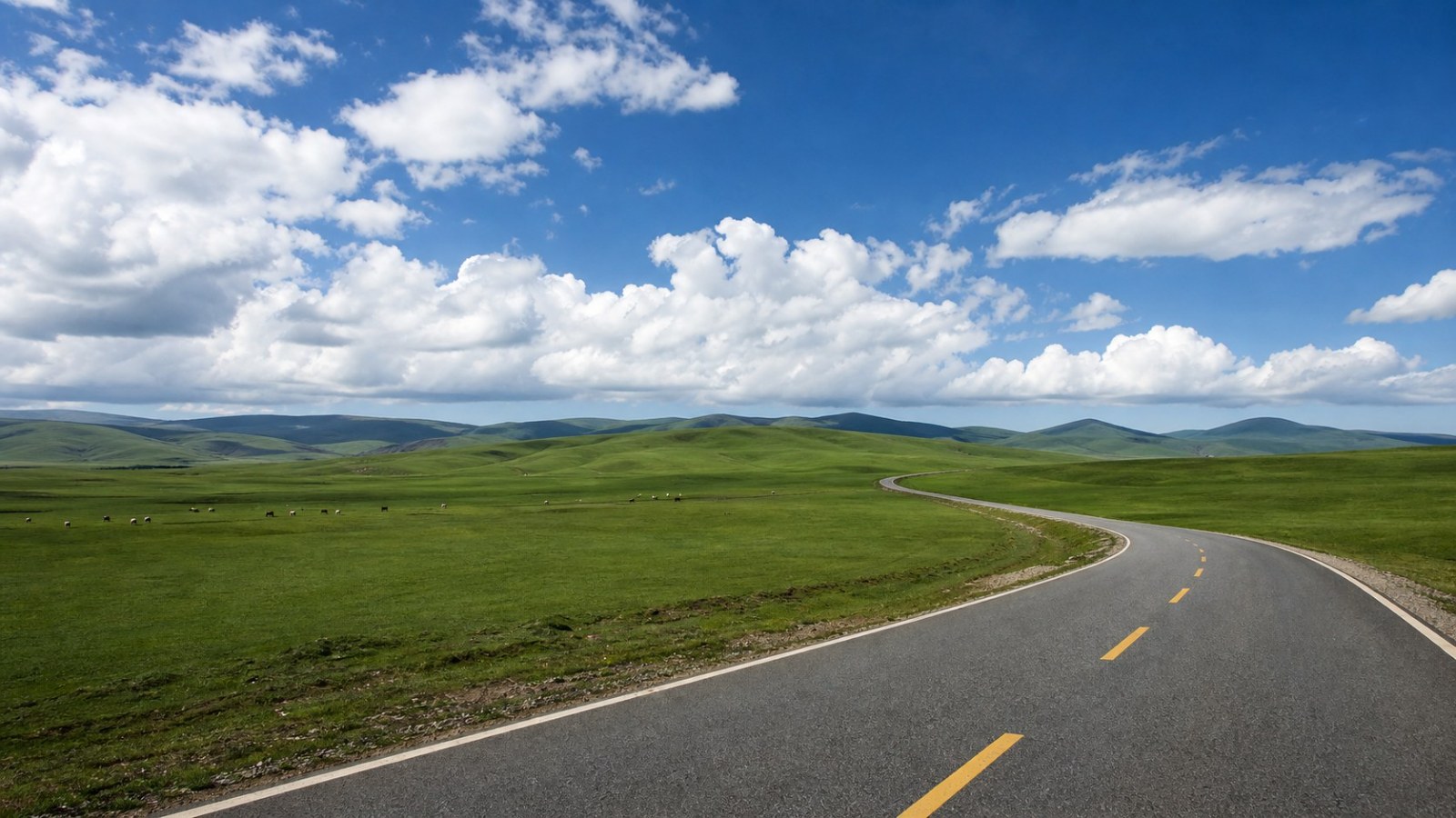 Scenic road crossing Gongger Grassland beneath a wide blue sky