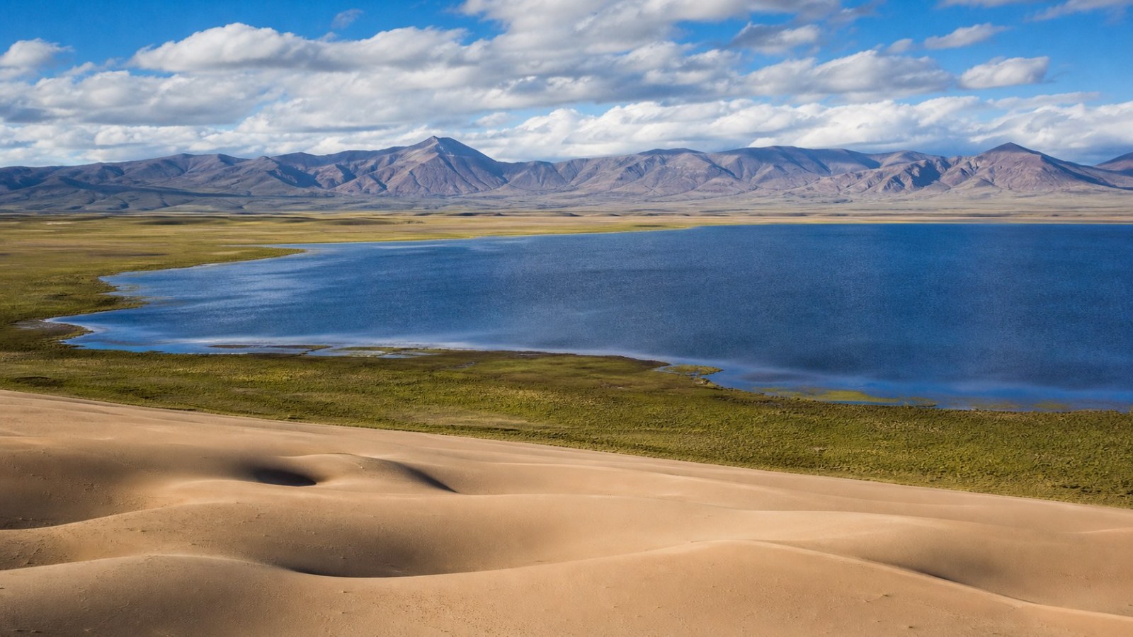 Rippled dunes beside blue water at Yulong Sand Lake