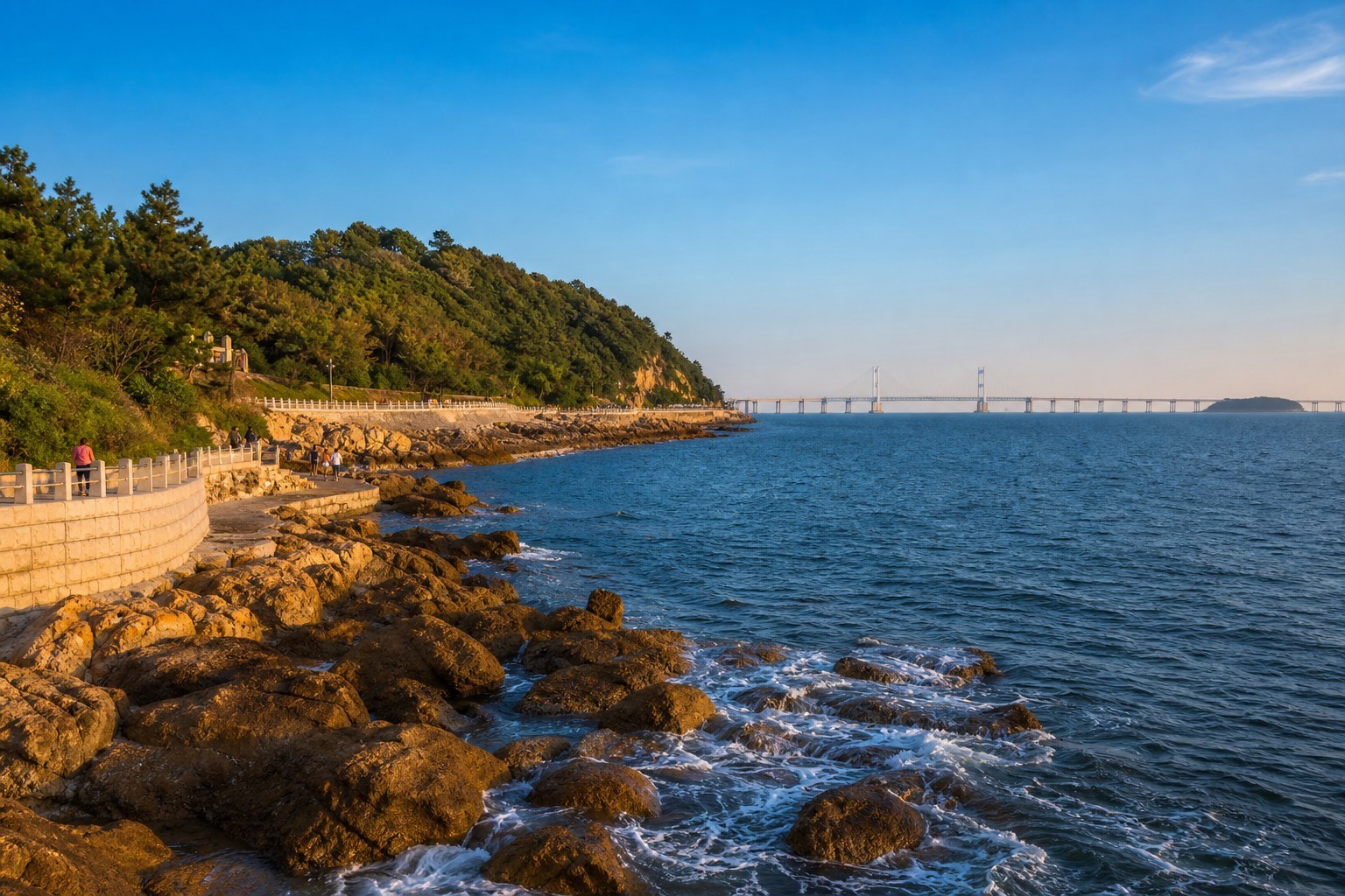 Wave-washed rocks, green headland and distant sea bridge along the Dalian coast