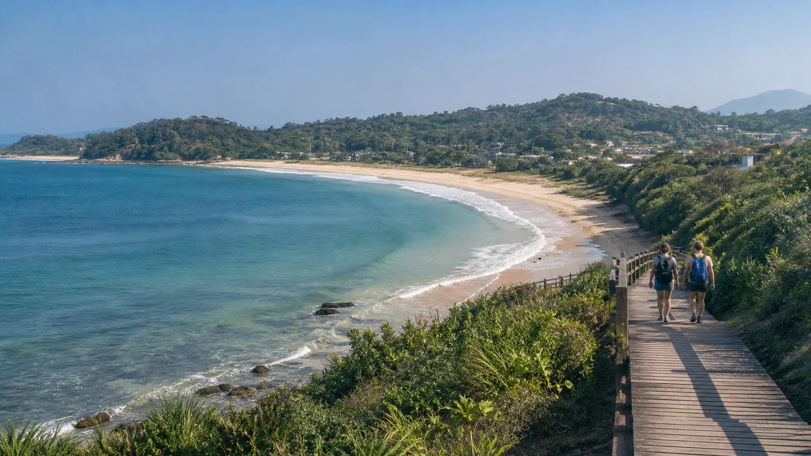 Travelers walk above a quiet curved beach on the Wanning coast