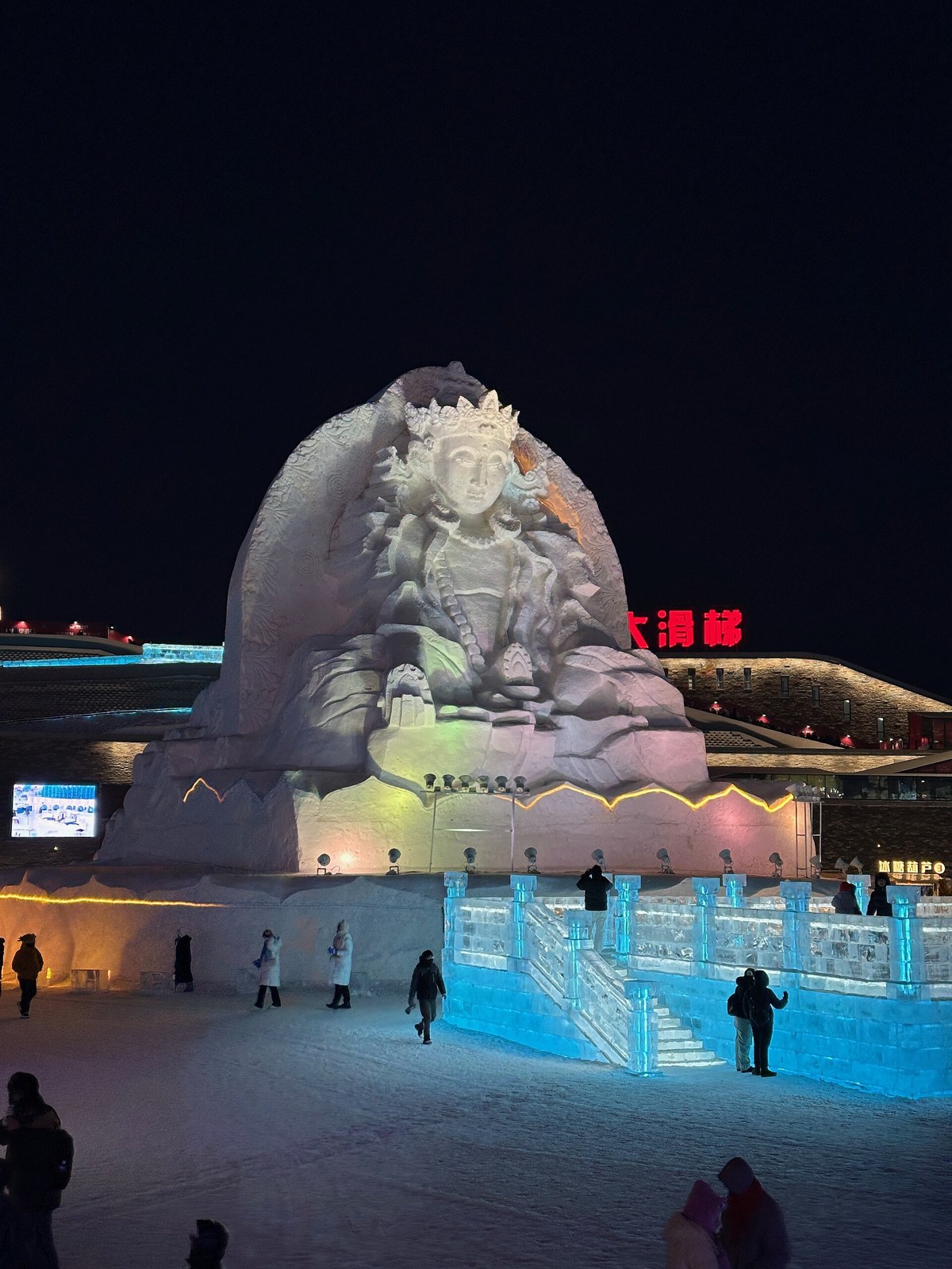 A large illuminated snow sculpture behind blue ice walls in Harbin