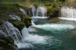 Water flowing between green trees and mossy rocks at Xiaoqikong in Libo