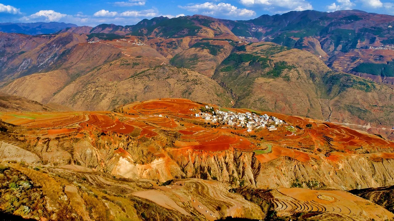 Red hillside fields surrounding a white village in a mountain valley in Dongchuan