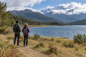 Two travelers looking across a lake toward wooded mountain slopes