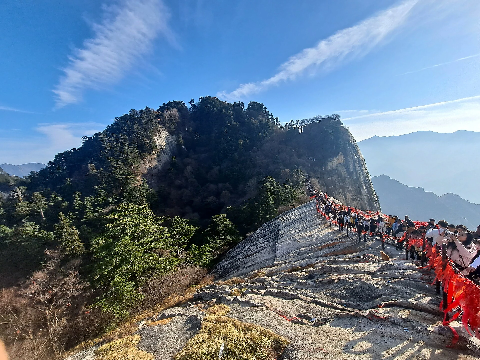 Visitors on a chained granite ridge beneath trees at Mount Huashan’s West Peak
