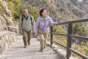 Two older travelers walking up stone steps beside a handrail