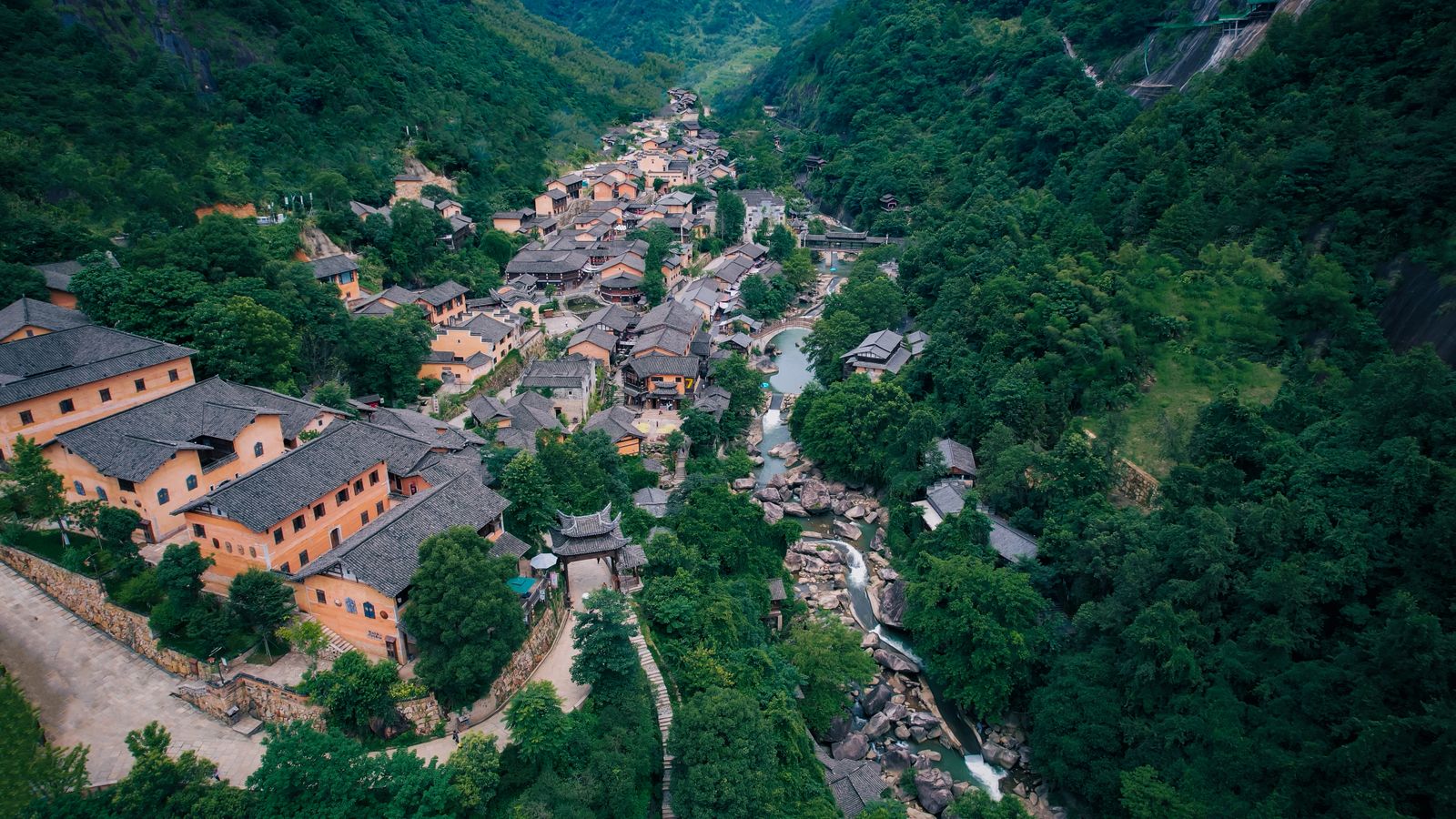 Traditional-style buildings beside a stream between wooded hills at Wangxian Valley